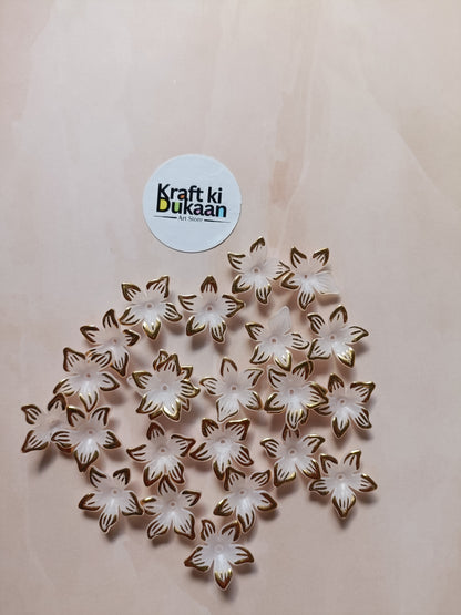 Flower bead charms, white flowers with gold outlines, scattered on surface