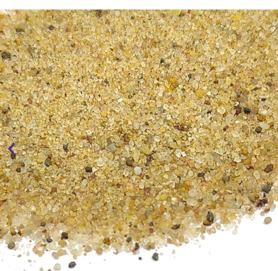 Close-up of natural sand granules, tan and yellow with small dark specks