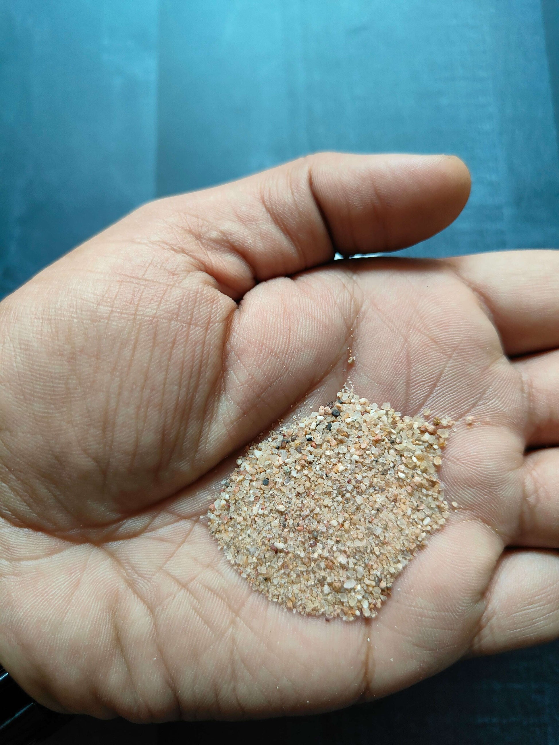 Natural sand grains in palm, light tan with mixed tiny pebbles