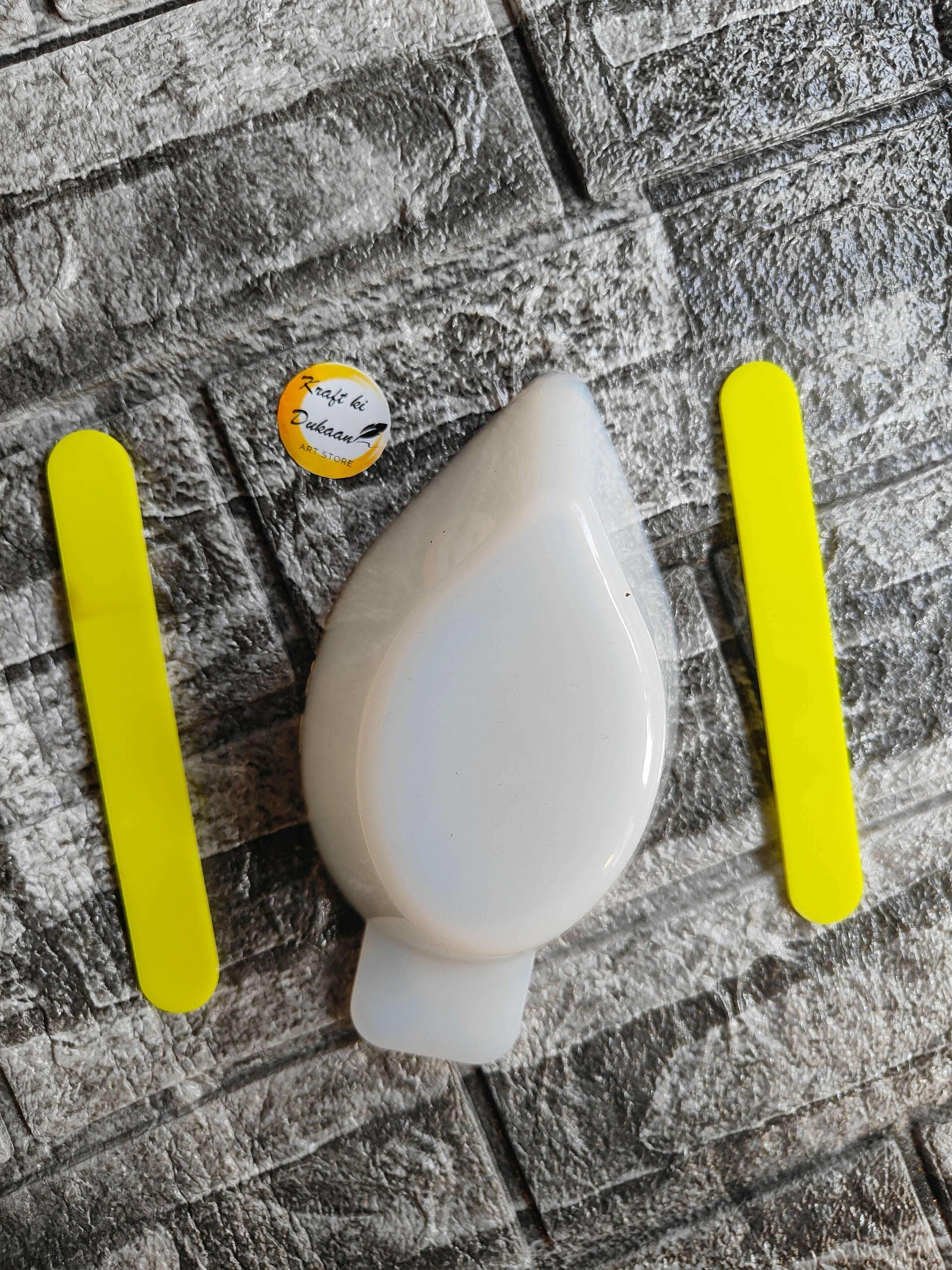 White silicone mixing cup with two yellow sticks beside it, oval pouring spout