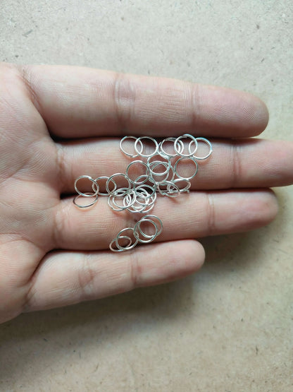 Assorted silver-tone circle metal rings held in a palm, open loop style.
