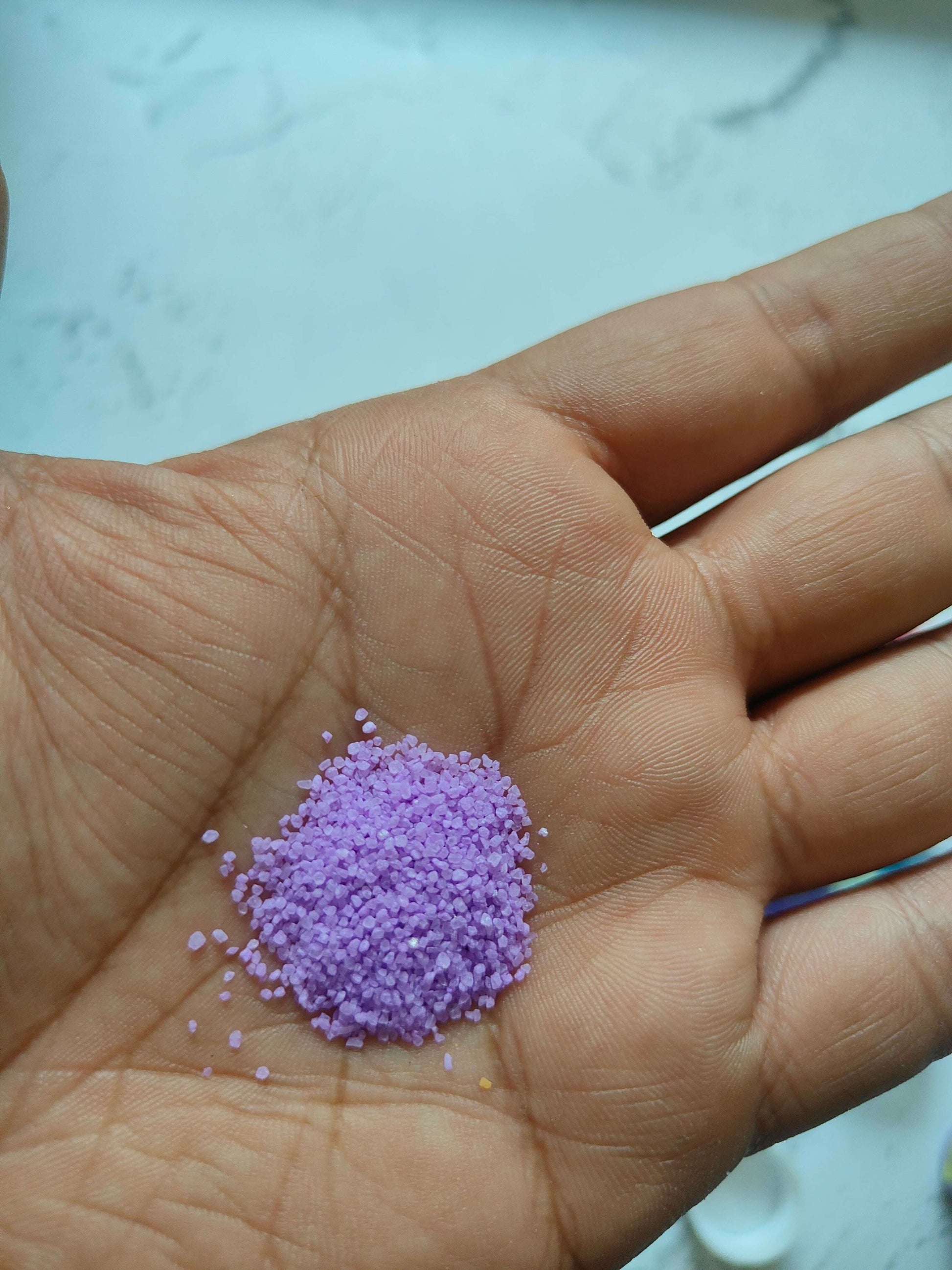 Hand with a small pile of purple colored sugar sand grains