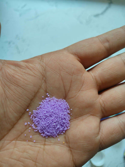 Hand with a small pile of purple colored sugar sand grains