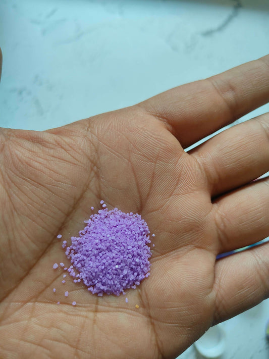 Hand with a small pile of purple colored sugar sand grains