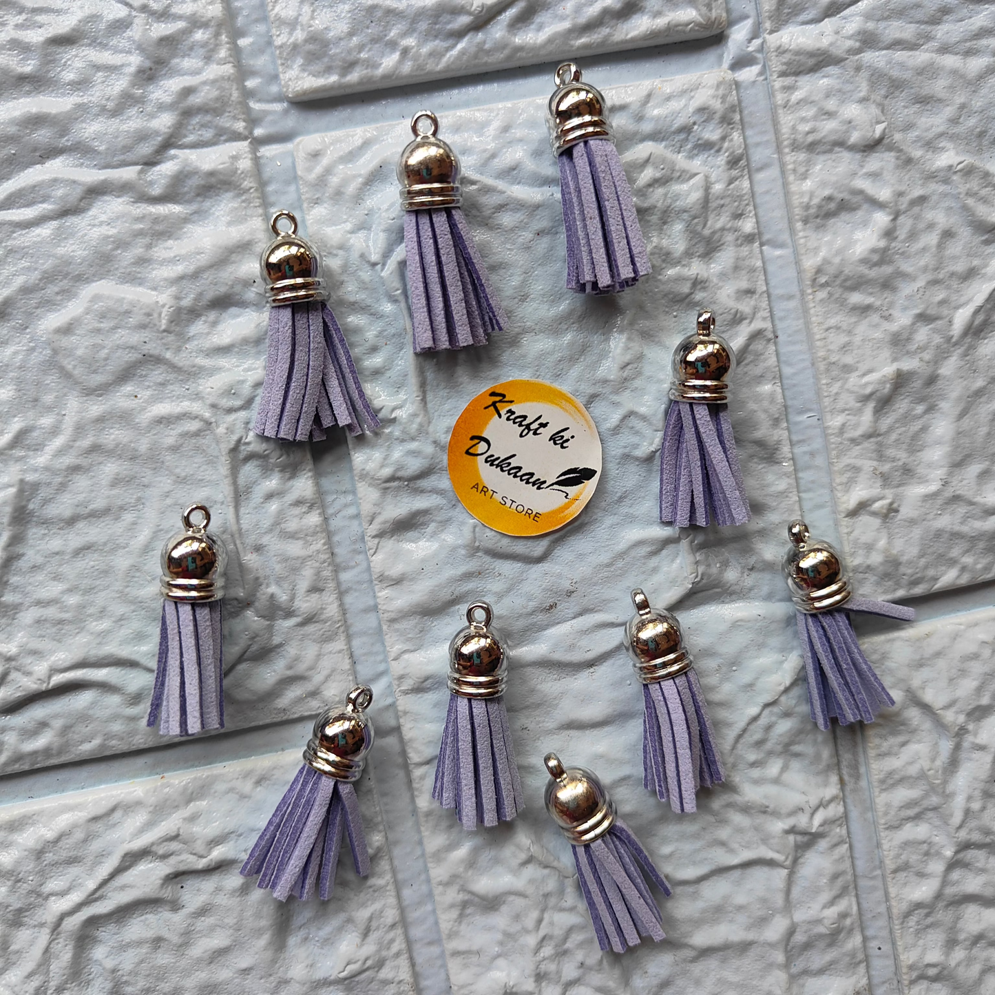 Set of silver leather tassel charms arranged on a textured surface for crafting projects