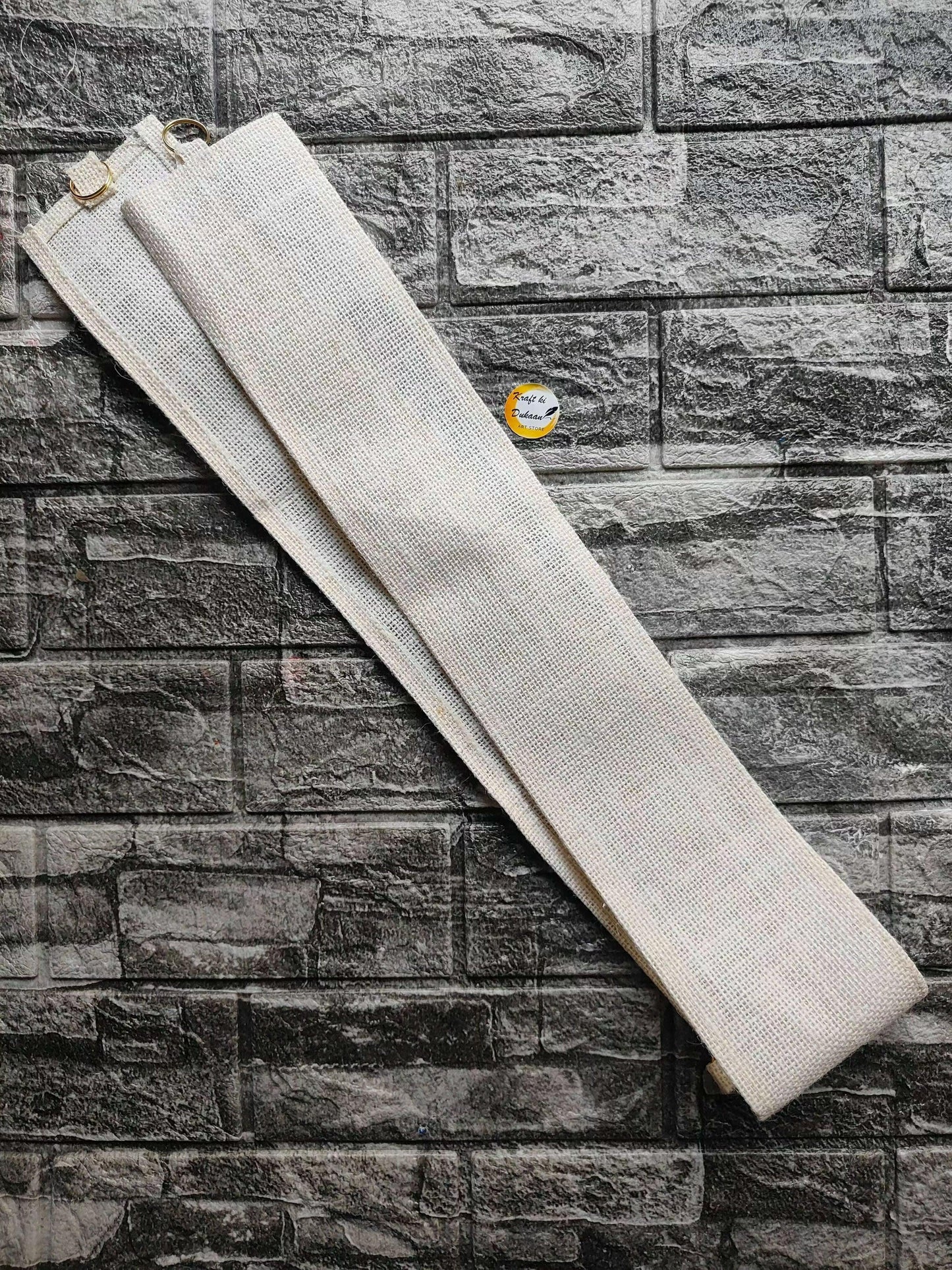 Toran belt with textured white fabric strap and small metal ring at one end