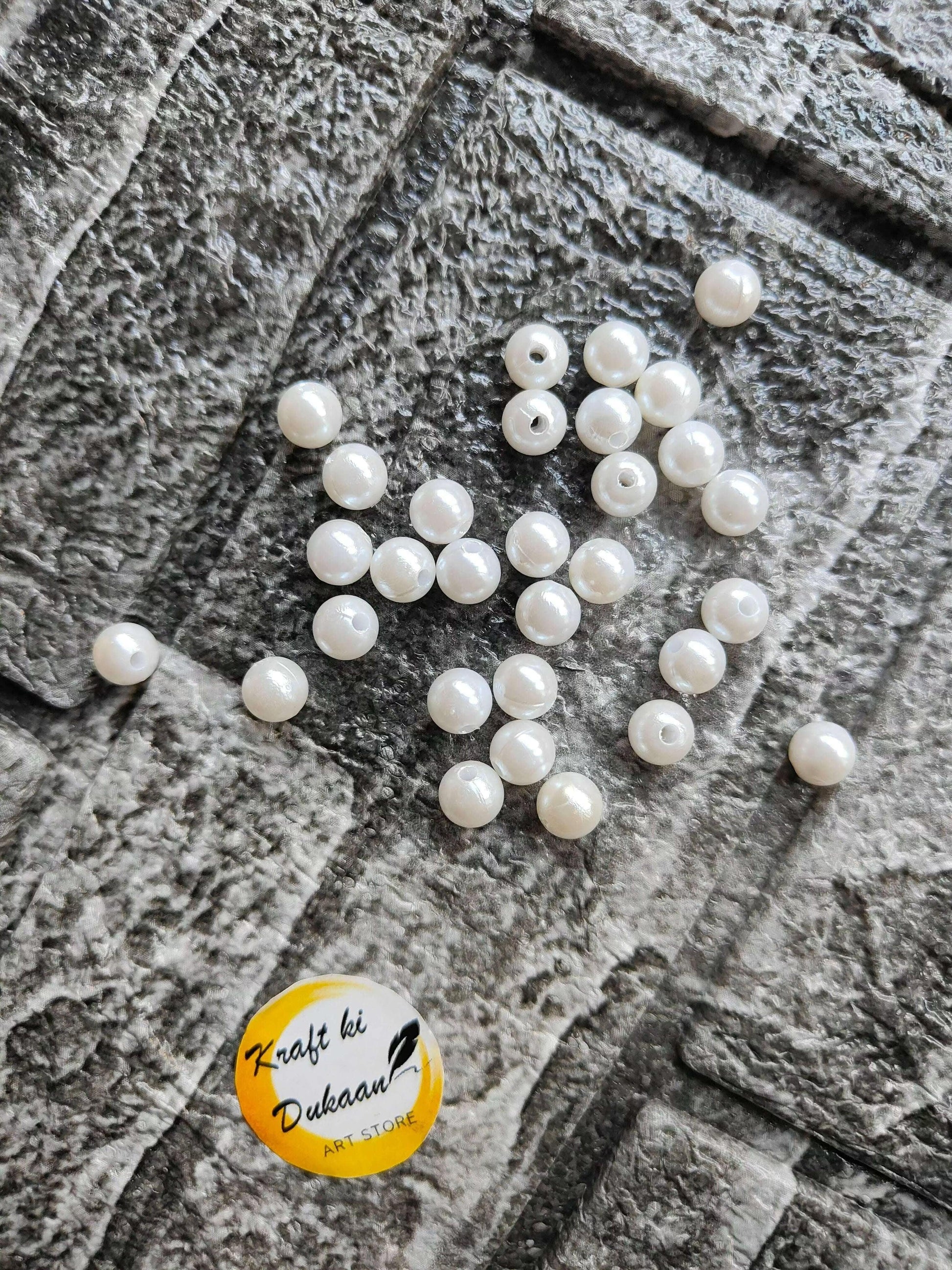 White pearl beads with drilled holes; loose group of round pearls on fabric